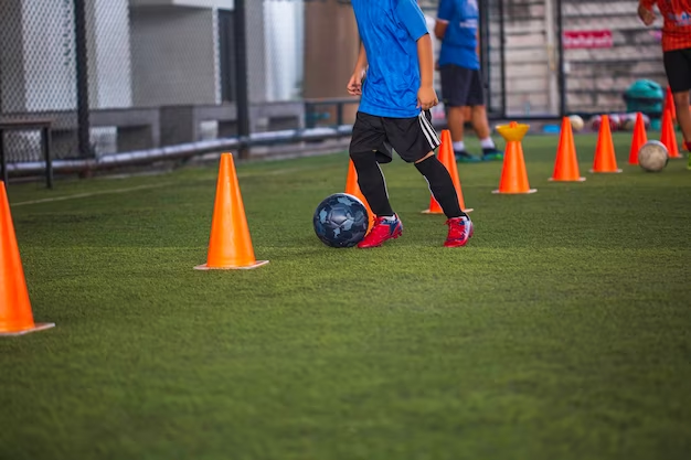 Football training with a person using orange road cones as obstacles on a field