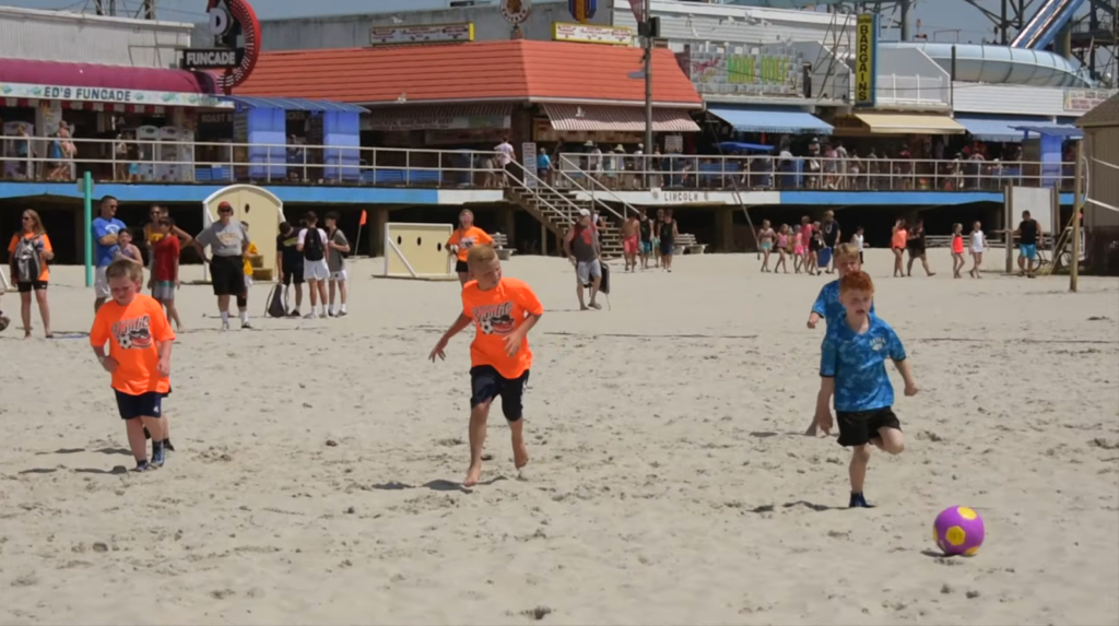 boys playing soccer on the beach, buildings with people behind