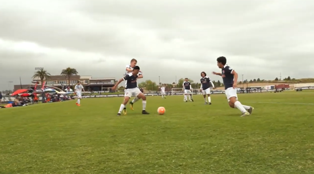 boys playing soccer on the field, one is passing the ball to another, palms behind